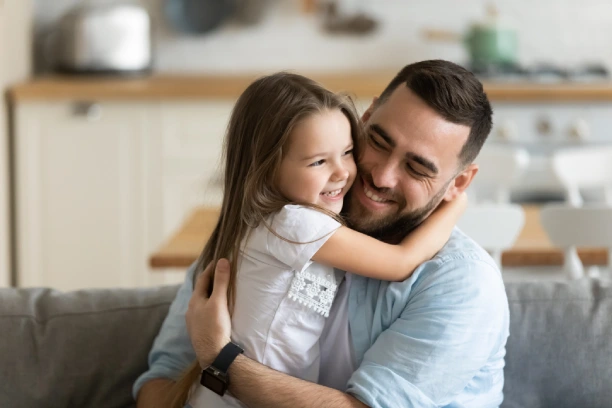 Father and daughter hugging on couch.